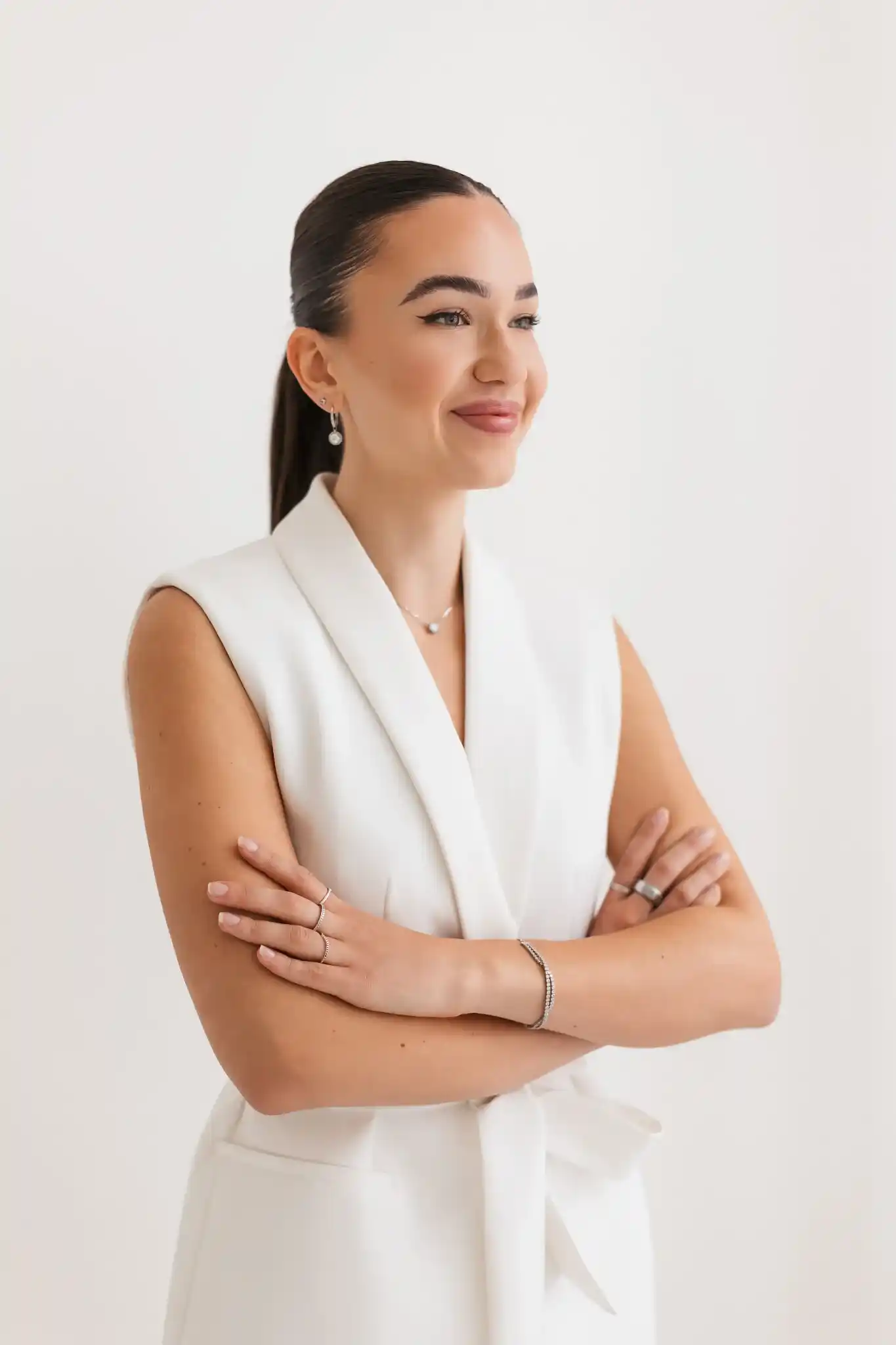 Erika Hudacova, PhD, in a white suit with her arms crossed, smiling