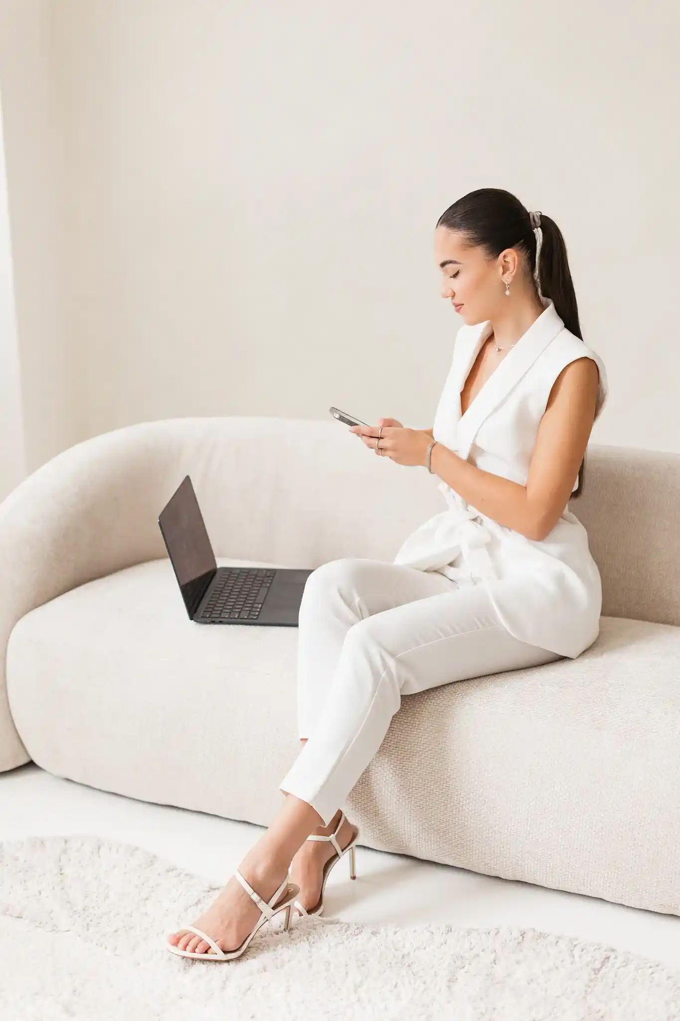 Erika in a white suit on the sofa with her phone